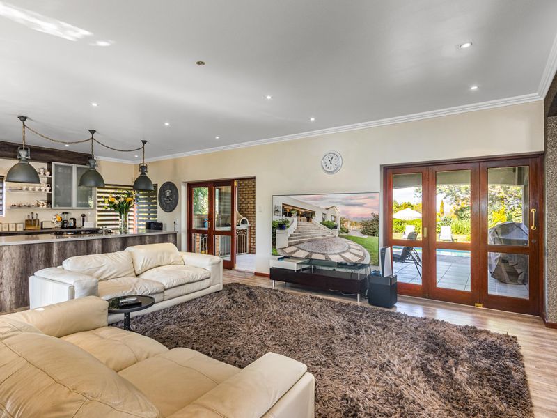 Spacious open-plan living area featuring a modern kitchen with breakfast bar, recessed lighting, and large wooden doors opening to the outdoor patio area.