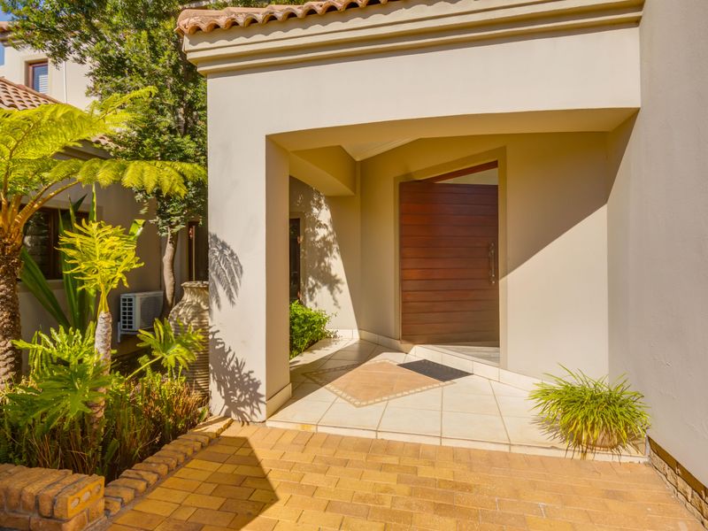 A welcoming covered entrance featuring a solid timber front door, tiled porch area, and paved walkway surrounded by established garden landscaping.