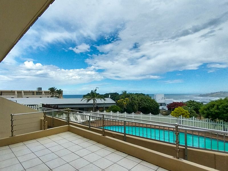 Spacious covered balcony featuring tiled flooring and a stainless steel balustrade, offering elevated views over the complex swimming pool and surrounding landscape.