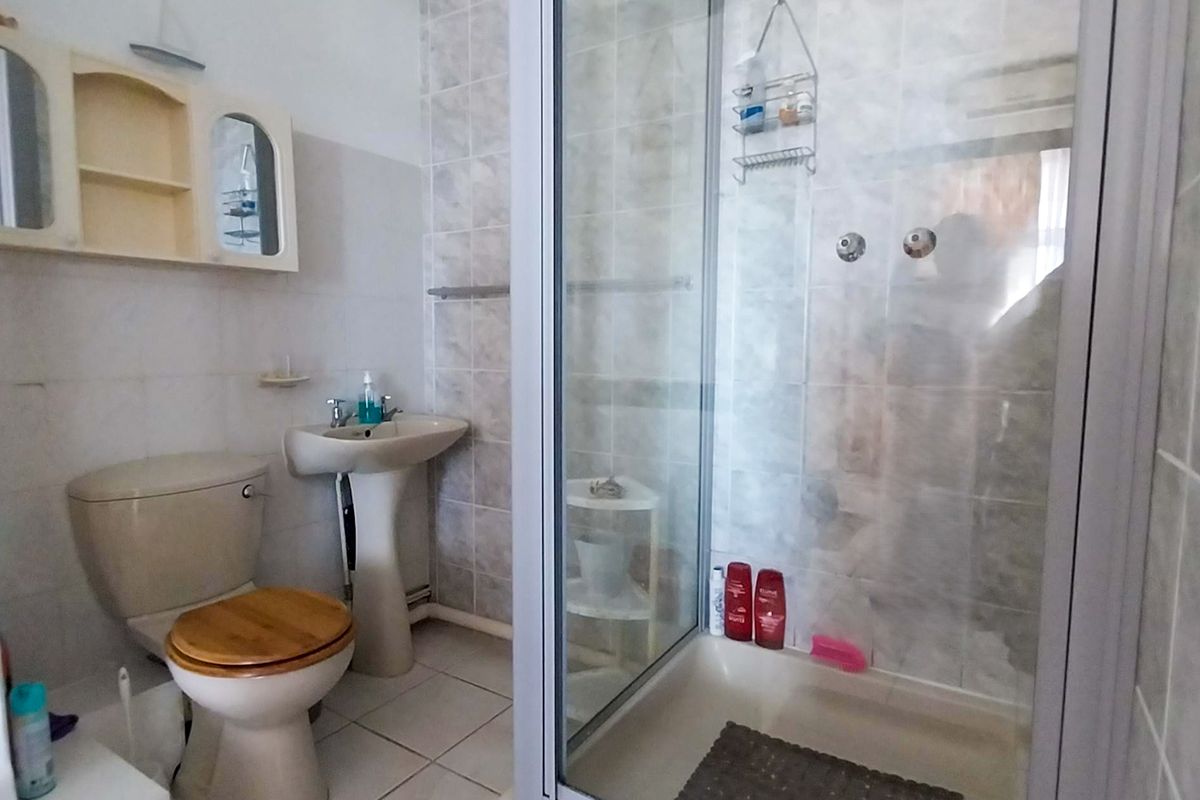 A functional bathroom featuring a pedestal sink, toilet, and a glass-enclosed shower with tiled walls and flooring.