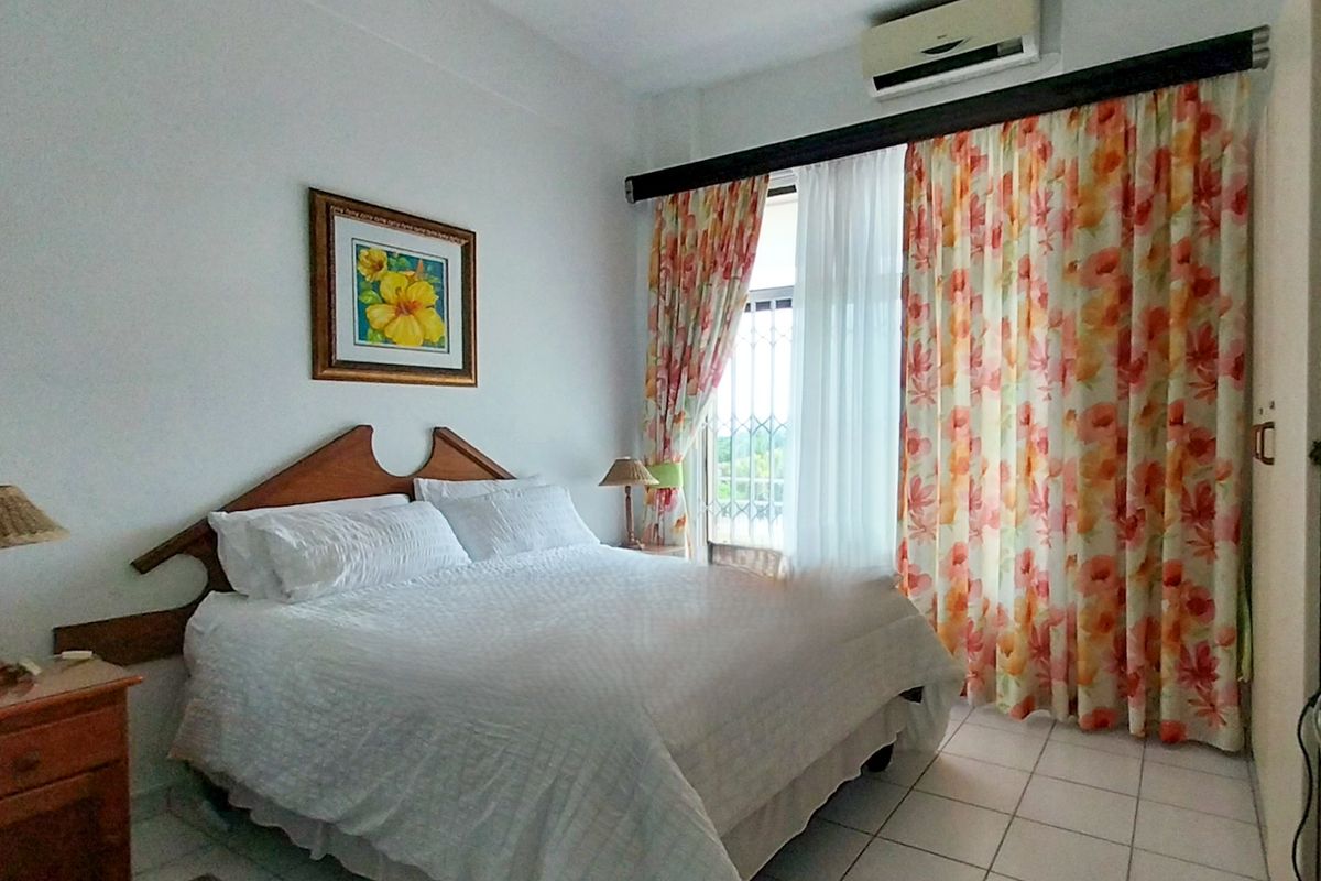 A functional bedroom featuring tiled flooring, a built-in wardrobe, and a wall-mounted air conditioning unit with access to a balcony.