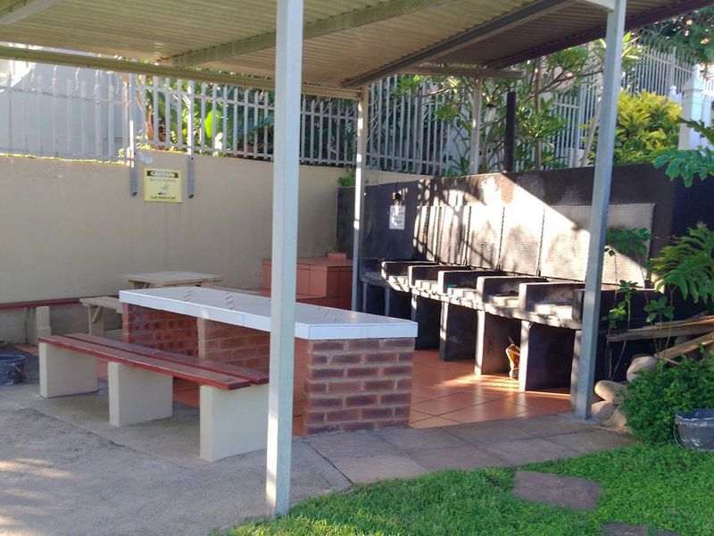 Outdoor communal entertainment area featuring a covered patio with a built-in braai station, tiled prep counter, and brick masonry seating.