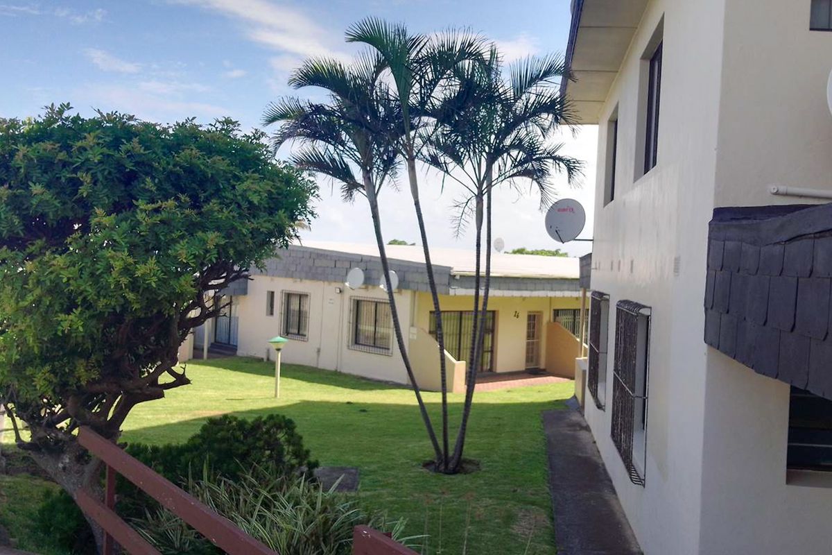 A view of the rear exterior of the apartment complex, featuring a shared garden area, paved walkways, and building facades with security bars.