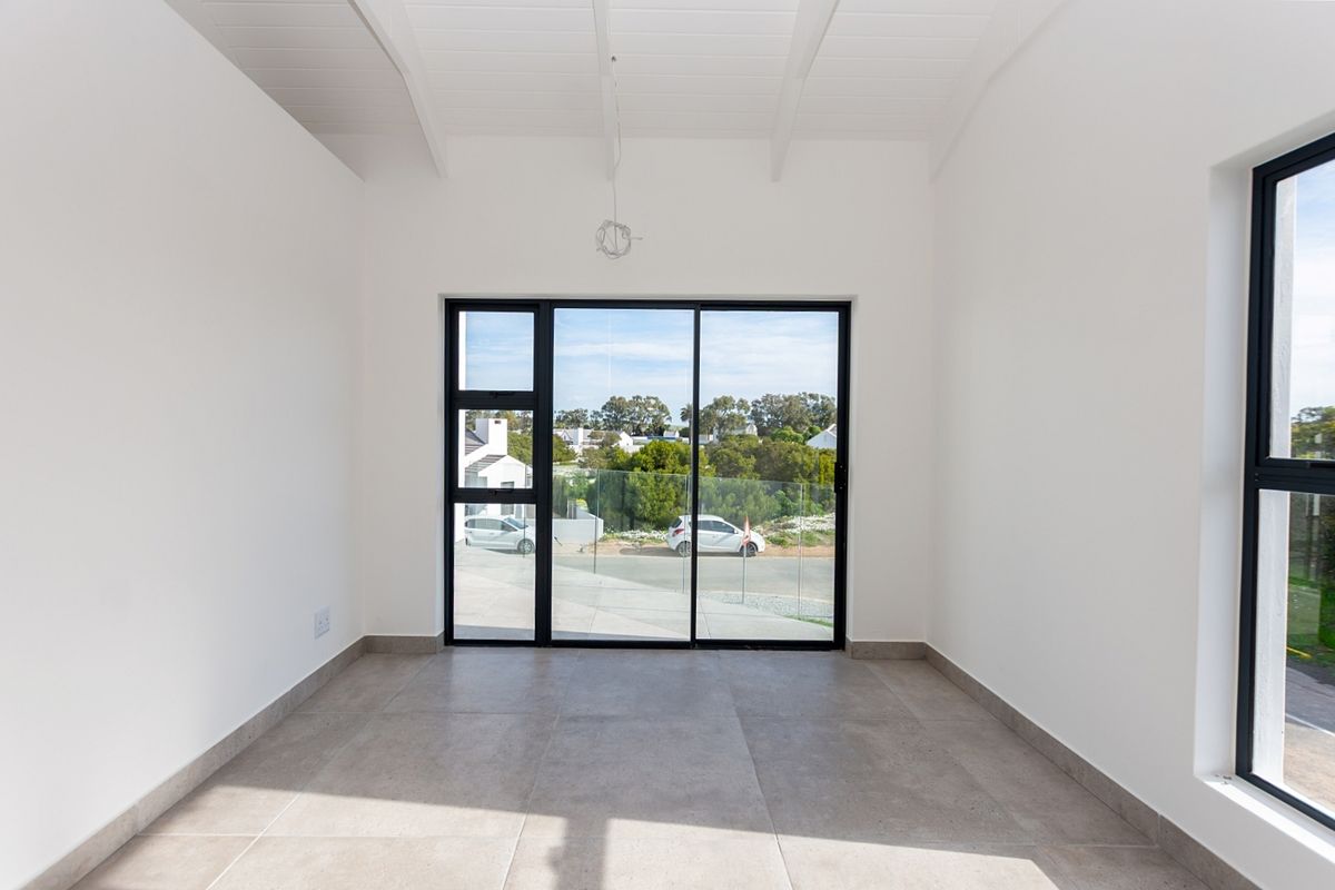 A bright, modern, empty living area featuring high exposed beam ceilings, large aluminium sliding doors, and neutral tiled flooring.