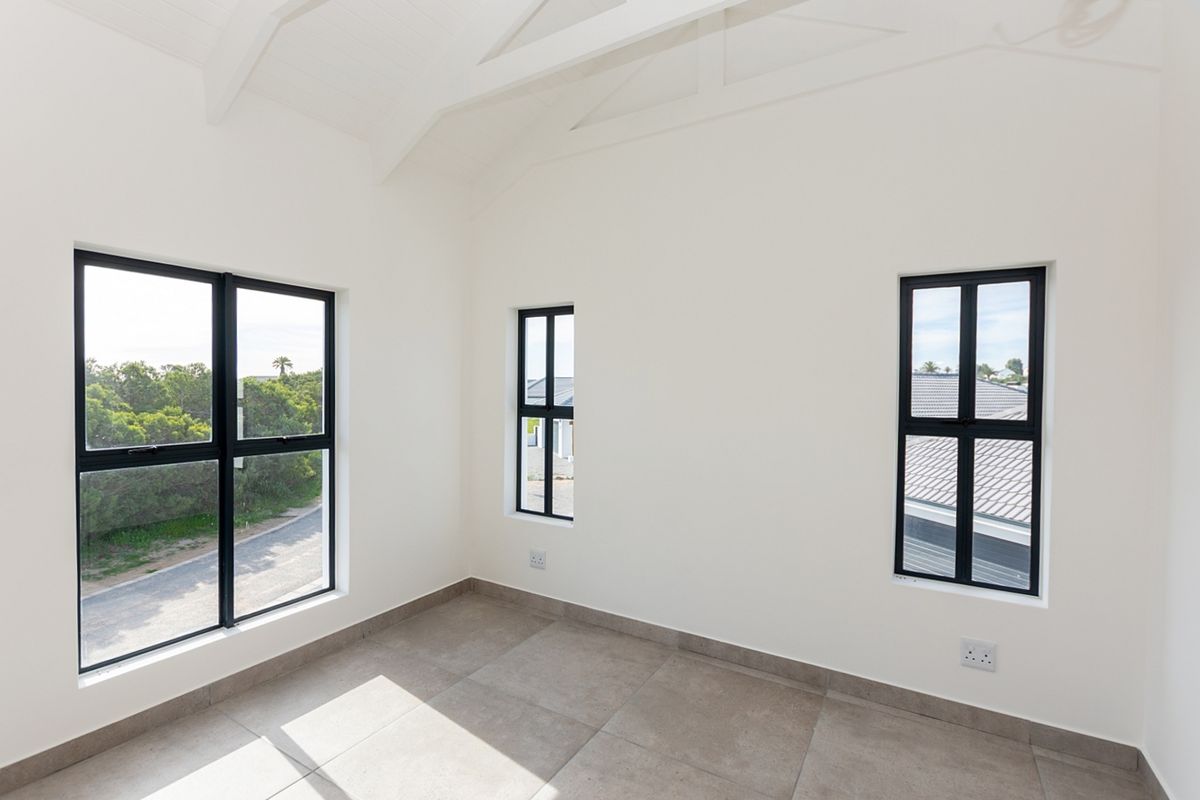 A bright, empty bedroom featuring vaulted ceilings with exposed rafters, modern tiled flooring, and large black-framed windows providing natural light.