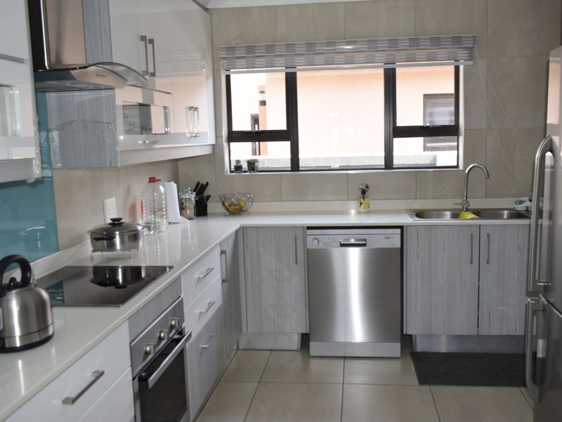 Modern kitchen featuring sleek white and grey cabinetry, stone countertops, integrated stainless steel appliances, and tiled splashbacks with ample natural light.