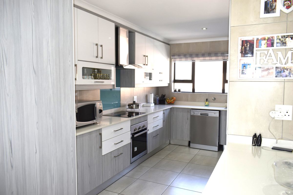 Modern kitchen featuring two-tone cabinetry, stone countertops, integrated electric hob, oven, extractor fan, and tiled flooring with ample natural light.