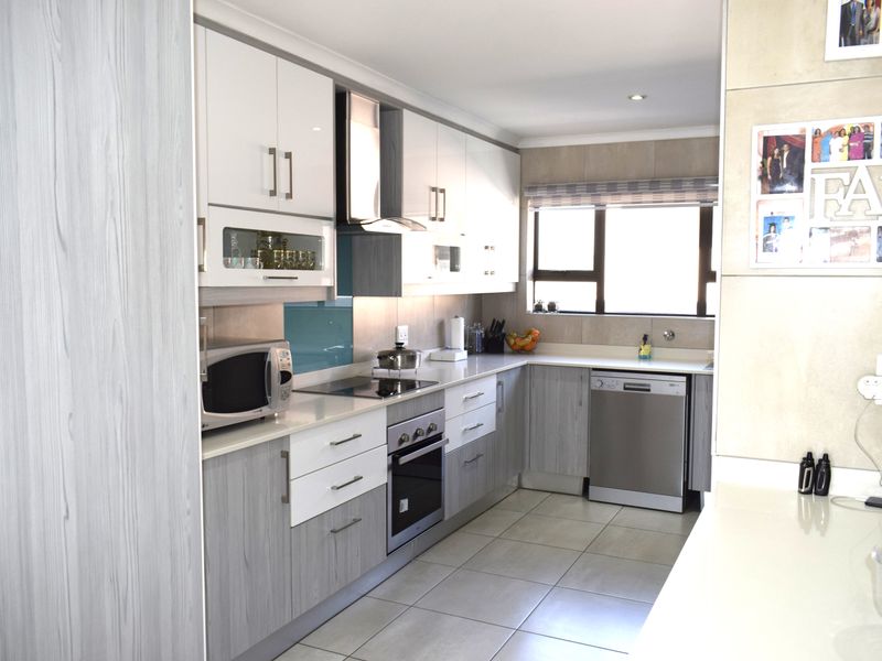 Modern kitchen featuring two-tone cabinetry, stone countertops, integrated electric hob, oven, extractor fan, and tiled flooring with ample natural light.