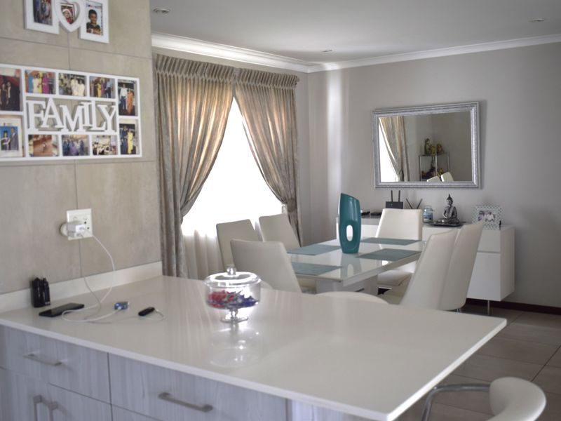 An open-plan living and dining area featuring a modern kitchen island with stone countertops, neutral tiled flooring, and recessed lighting throughout.