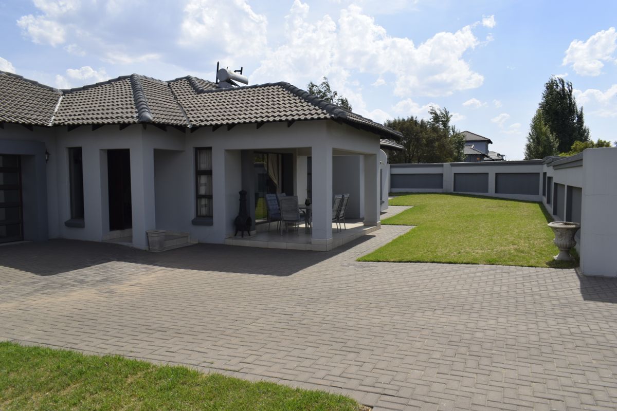 Rear view of the property featuring a paved driveway, covered patio area, well-maintained lawn, and secure boundary walling.