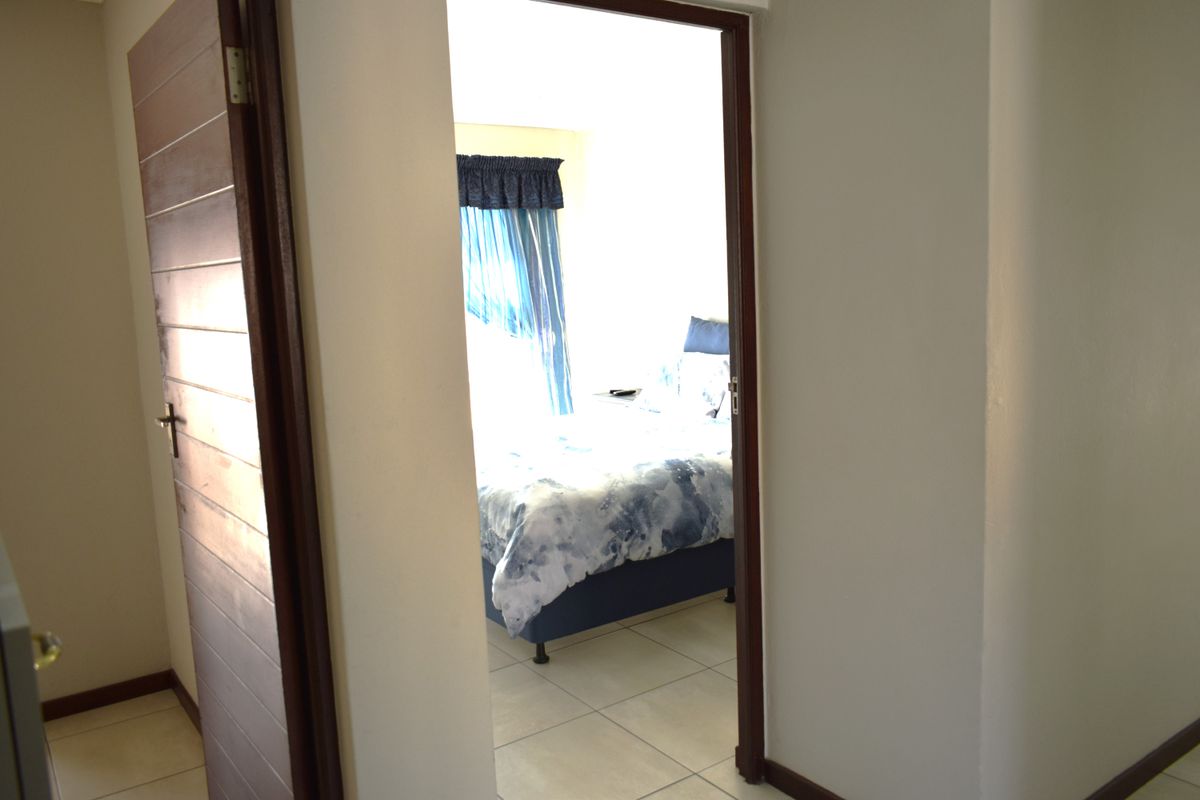 A view through a wooden doorway into a bedroom featuring tiled flooring and natural light.