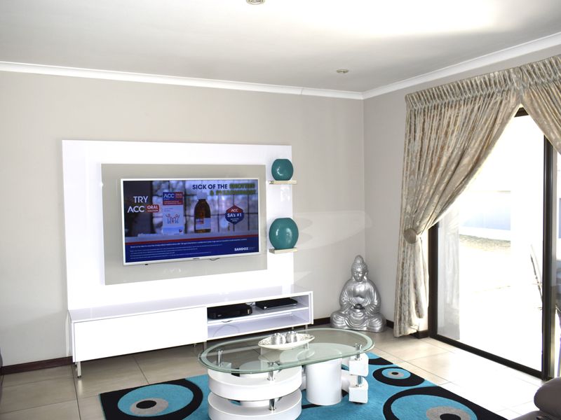 A bright living room featuring a modern built-in media unit, tiled flooring, and a large sliding glass door providing access to the outdoors.