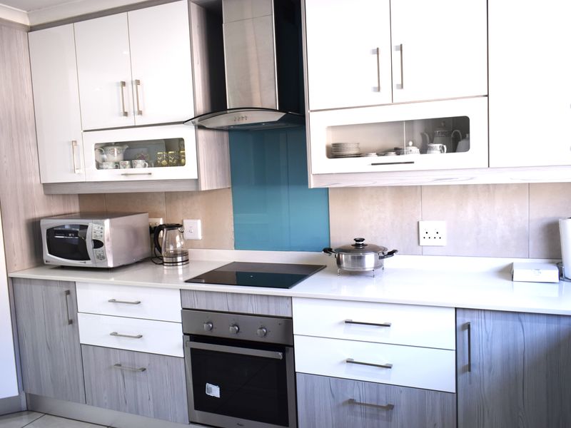 Modern kitchen featuring two-tone cabinetry, stone countertops, integrated electric hob, built-in oven, and a sleek glass splashback.