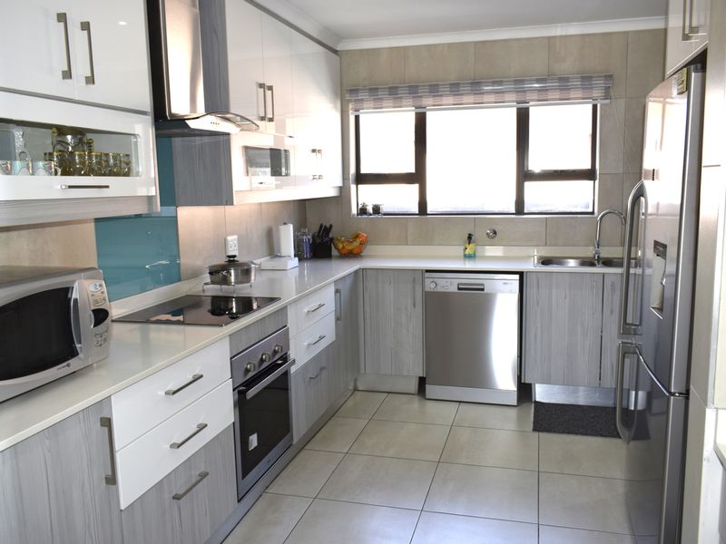 Modern kitchen featuring sleek two-tone cabinetry, stone countertops, integrated appliances, and tiled flooring with ample natural light.