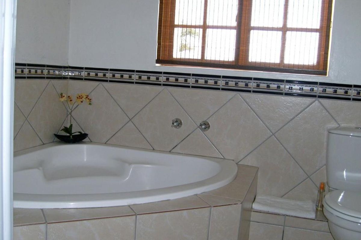 A functional bathroom featuring a corner bathtub, tiled surround with decorative accents, and a standard toilet.