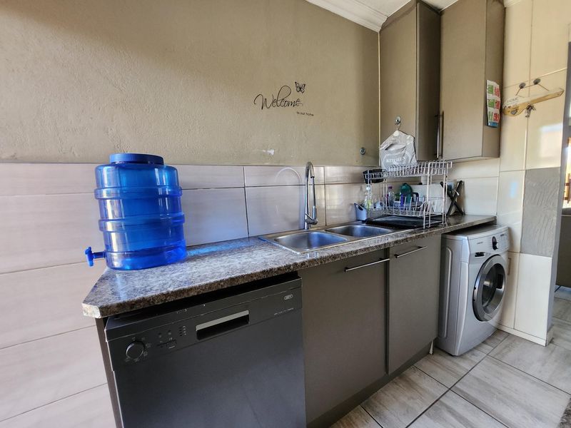 A functional laundry area featuring built-in cabinetry, a double bowl stainless steel sink, tiled backsplash, and space for a dishwasher and washing machine.