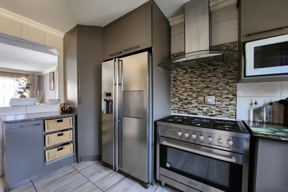 Modern kitchen featuring dark cabinetry, stone countertops, a gas stove with stainless steel extractor, and a mosaic tile backsplash.