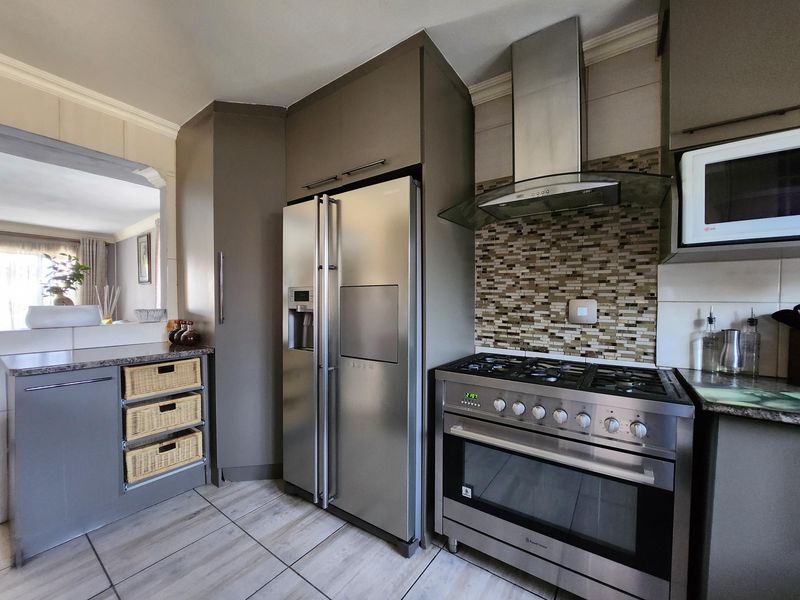 Modern kitchen featuring dark cabinetry, stone countertops, a gas stove with stainless steel extractor, and a mosaic tile backsplash.