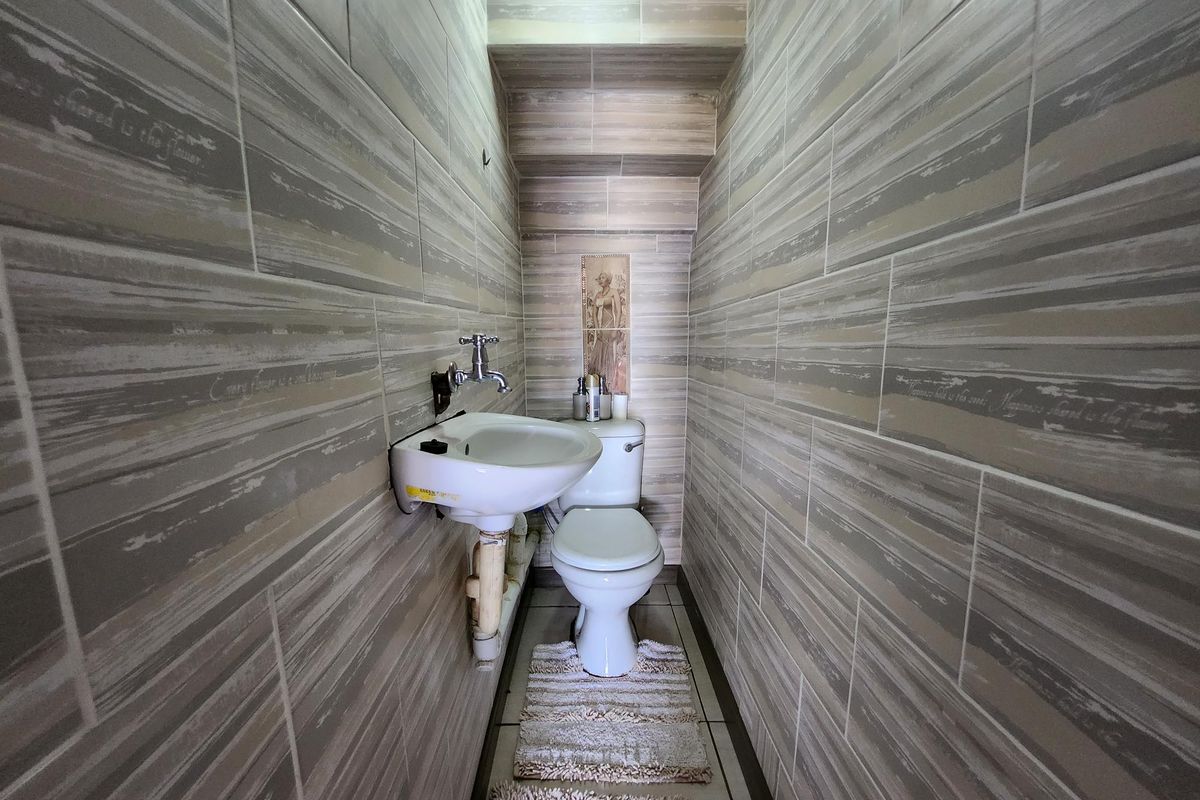 A compact guest bathroom featuring floor-to-ceiling decorative ceramic wall tiles, a wall-mounted basin, and a standard toilet.