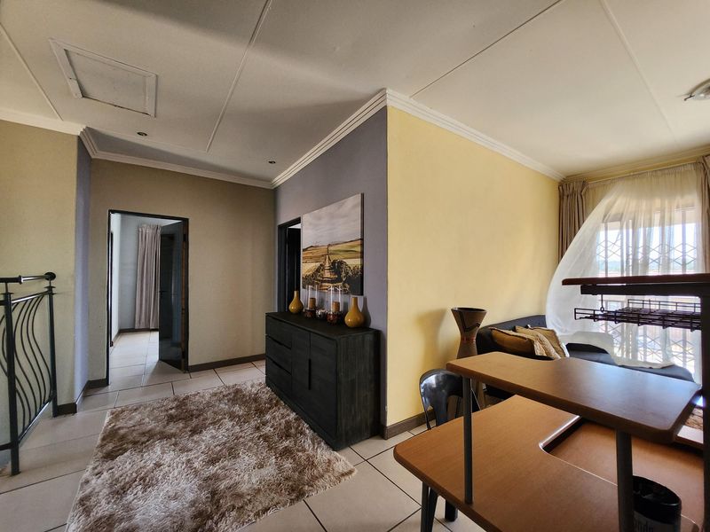 A living area featuring tiled flooring, coved ceilings, and access to an adjacent hallway, providing a functional and open layout.
