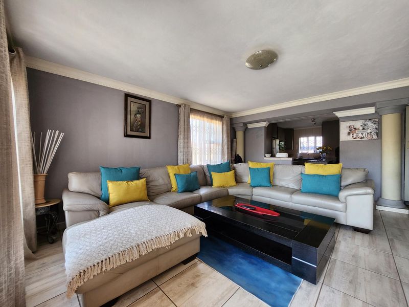 An open-plan living area featuring tiled flooring, crown molding, and a neutral wall finish, seamlessly connecting to the adjacent kitchen space.