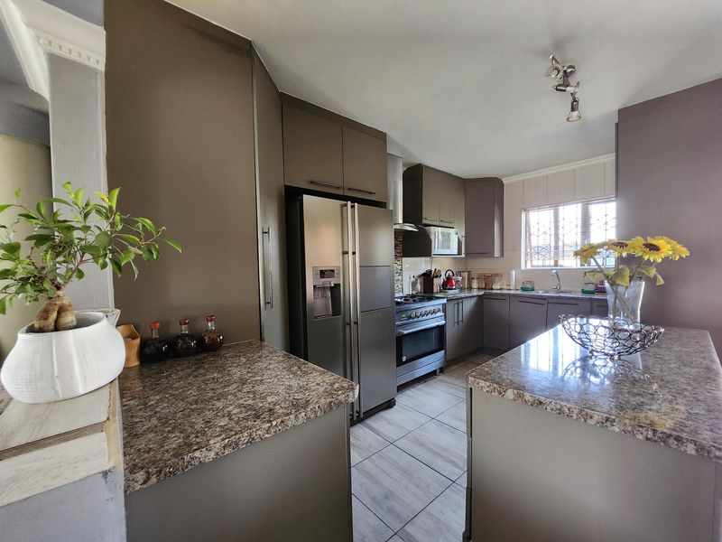 Modern kitchen featuring dark cabinetry, granite countertops, stainless steel appliances, and tiled flooring with a functional layout.