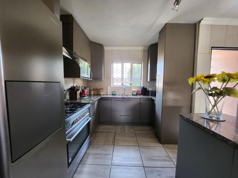 A modern kitchen featuring sleek cabinetry, granite countertops, a gas stove with extractor fan, and tiled flooring, offering a functional and well-maintained workspace.