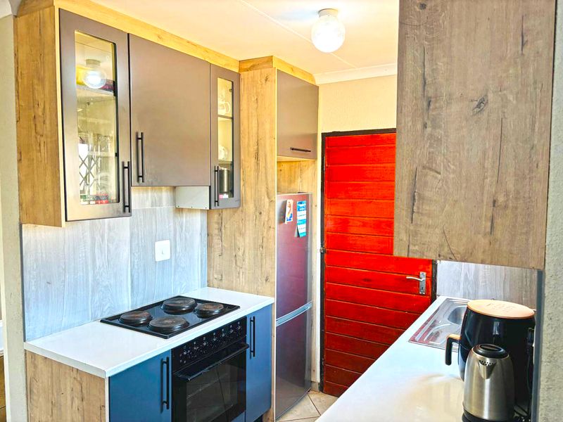 A compact kitchen featuring modern two-tone cabinetry, built-in oven and hob, laminate countertops, and a tiled backsplash.