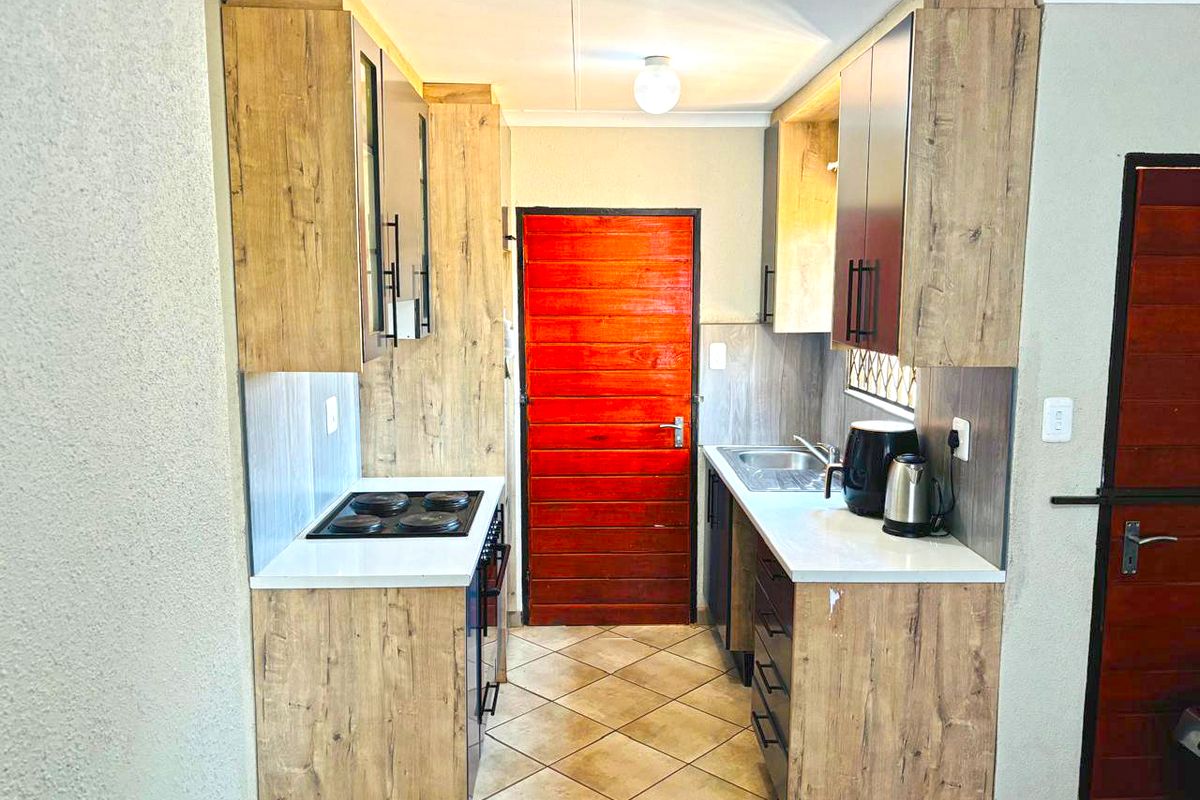 A compact galley-style kitchen featuring wood-look cabinetry, laminate countertops, an integrated electric hob, and tiled flooring.