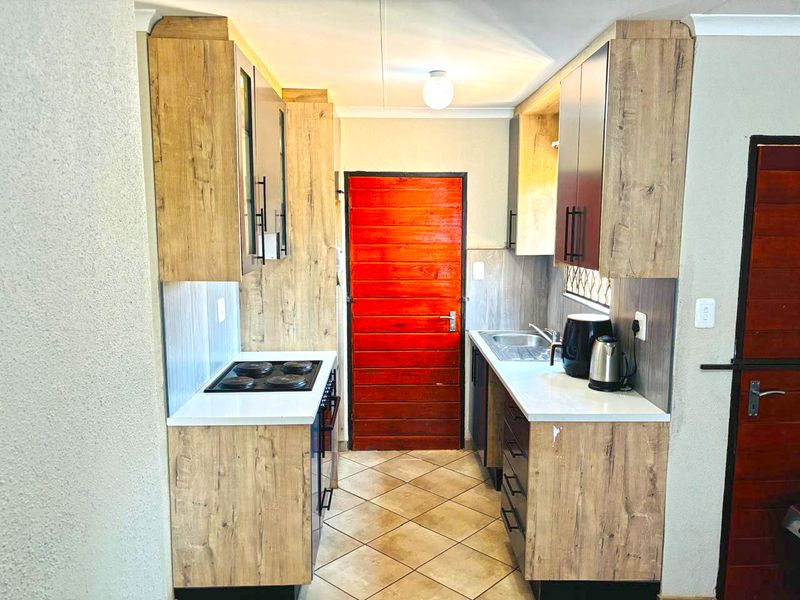 A compact galley-style kitchen featuring wood-look cabinetry, laminate countertops, an integrated electric hob, and tiled flooring.