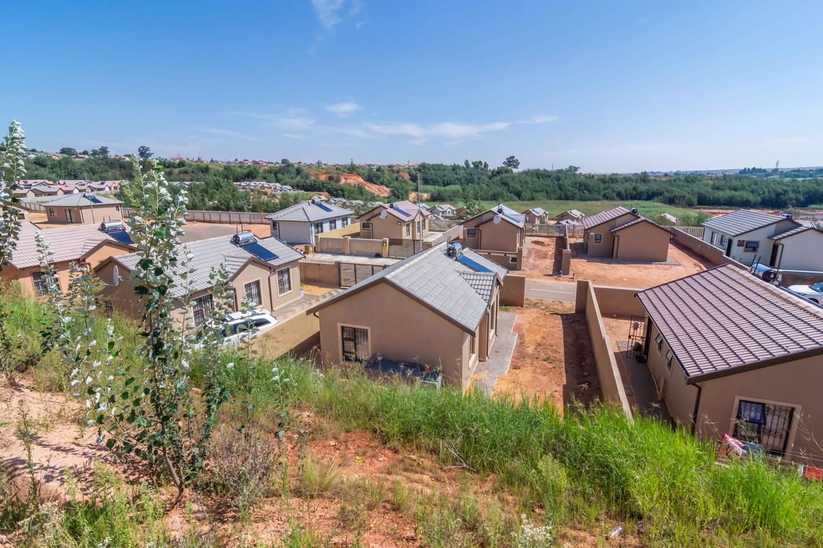 An elevated aerial view of a residential housing development featuring multiple detached homes with tiled roofs, solar water heaters, and perimeter boundary walls.