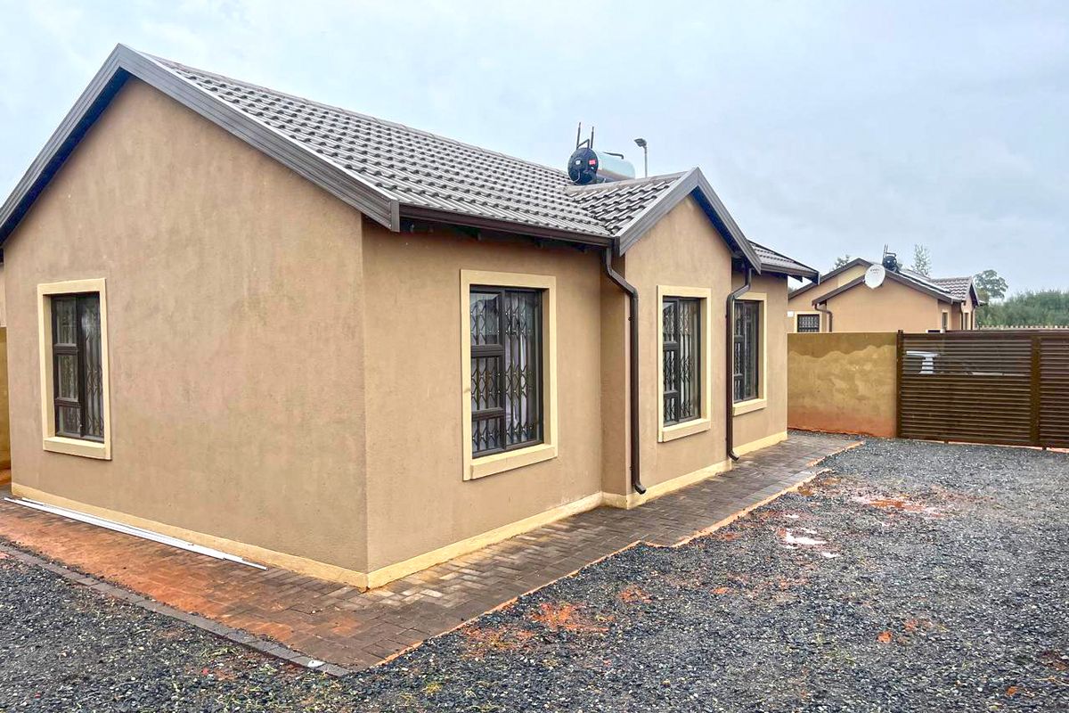 Rear view of a modern single-story house featuring a tiled roof, solar geyser, security bars on windows, and a paved walkway surrounding the structure.