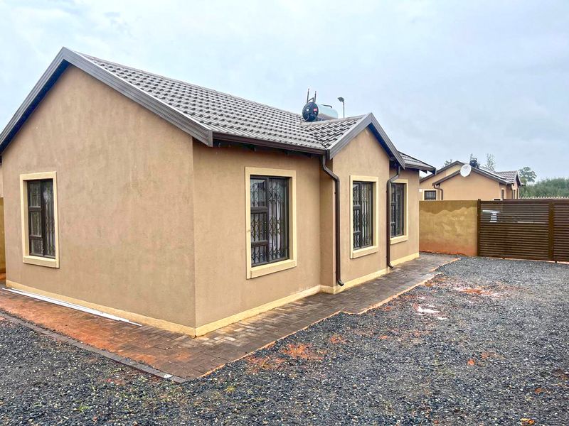 Rear view of a modern single-story house featuring a tiled roof, solar geyser, security bars on windows, and a paved walkway surrounding the structure.