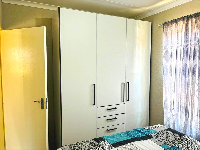 A bedroom featuring a modern white built-in wardrobe with integrated drawers and a neutral color scheme.