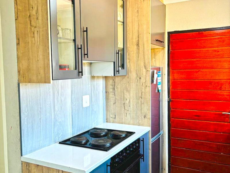 A compact kitchen featuring modern wood-look and blue cabinetry, an integrated electric hob and oven, and durable tiled flooring.