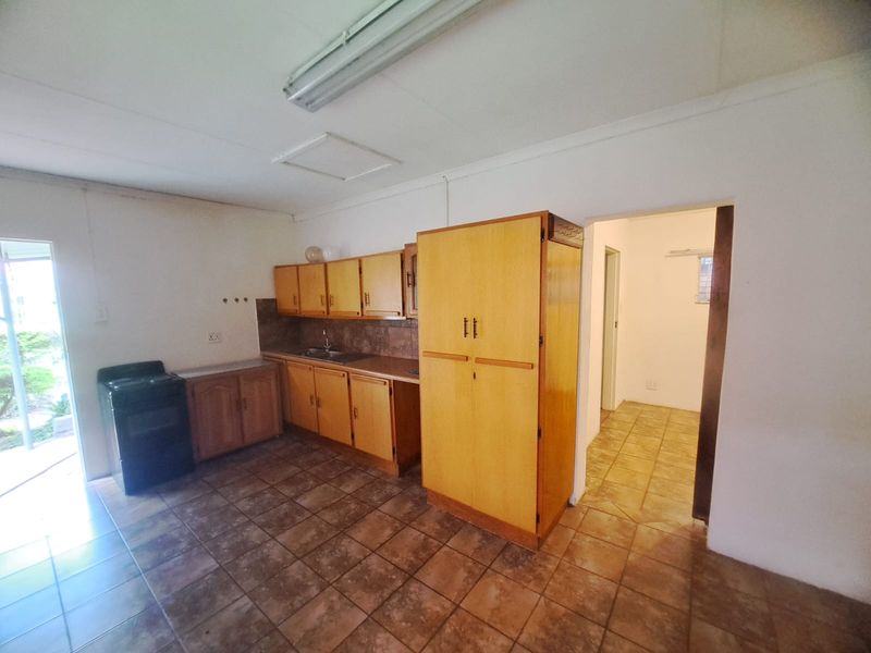 A functional kitchen featuring dated wooden cabinetry, laminate countertops, a stainless steel sink, and tiled flooring, offering potential for modernization.