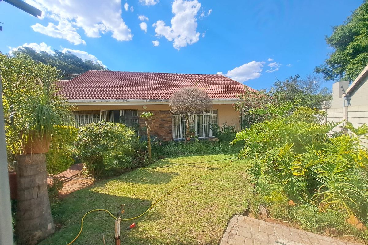 Rear view of the house featuring a tiled roof, stone cladding accents, security bars on windows, and a landscaped garden with a paved walkway.