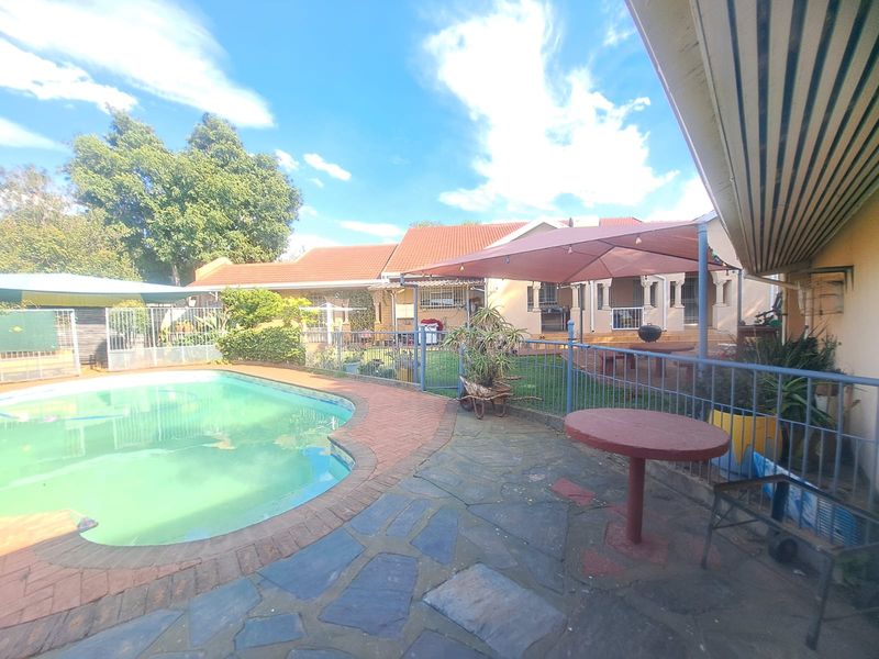 Outdoor entertainment area featuring a swimming pool, stone patio, and covered patio space, set within a fenced garden with established landscaping.