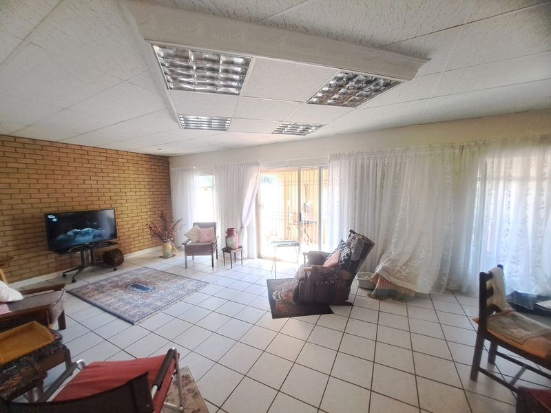 Spacious living room featuring an exposed brick feature wall, tiled flooring, and a drop ceiling with integrated fluorescent lighting, leading to a patio area.