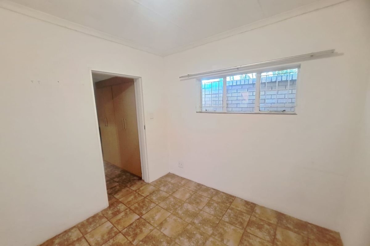 An empty bedroom featuring tiled flooring, built-in cupboards, and a window with security bars.