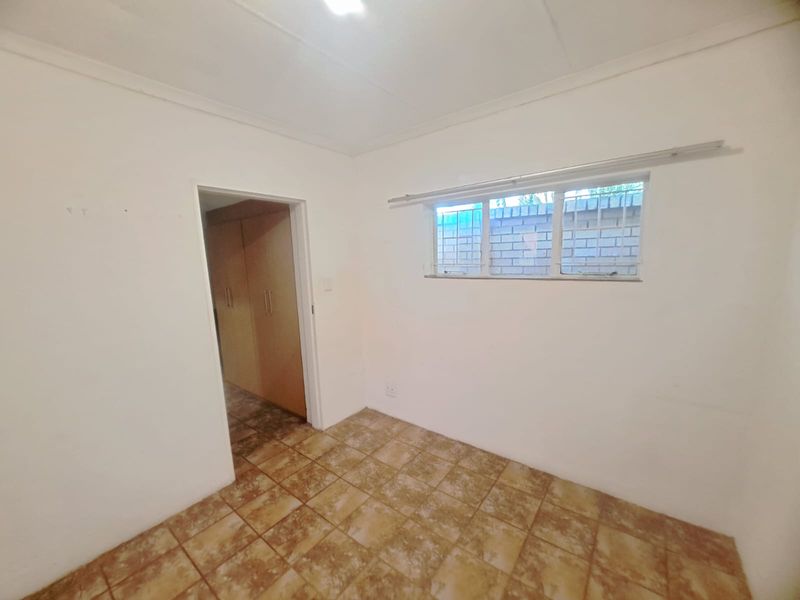 An empty bedroom featuring tiled flooring, built-in cupboards, and a window with security bars.