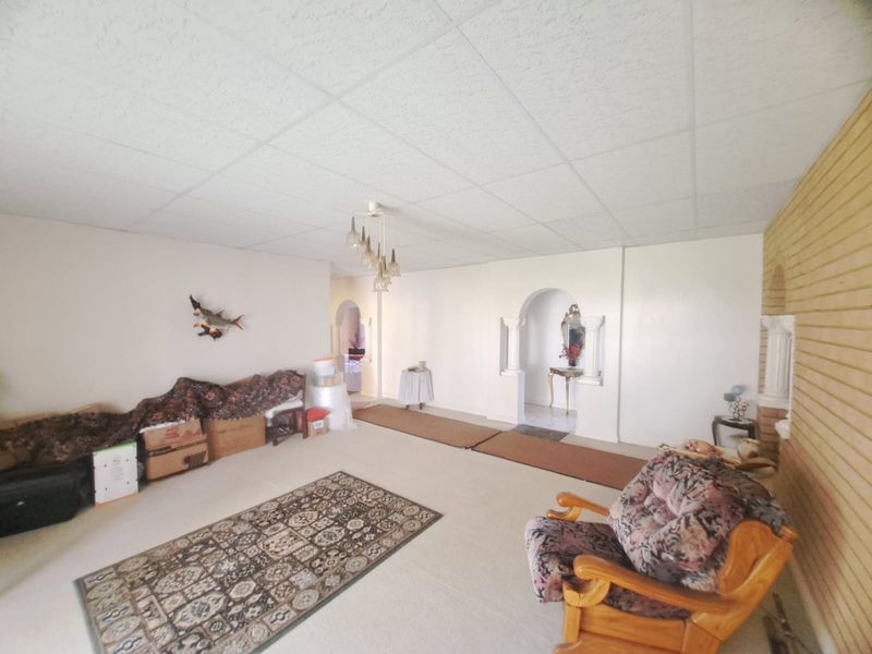 Spacious living area featuring a drop ceiling, arched architectural details, and a brick feature wall, offering a dated but versatile layout.