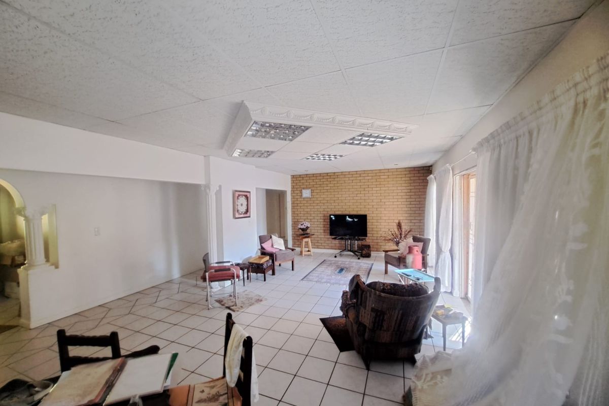 Spacious living area featuring tiled flooring, an exposed brick feature wall, and a dropped ceiling with integrated lighting, opening to an outdoor space.