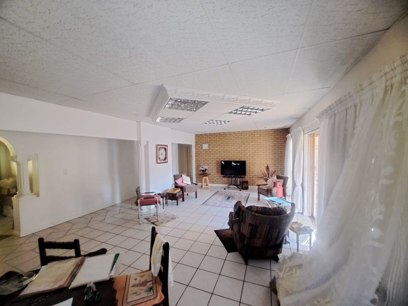 Spacious living area featuring tiled flooring, an exposed brick feature wall, and a dropped ceiling with integrated lighting, opening to an outdoor space.