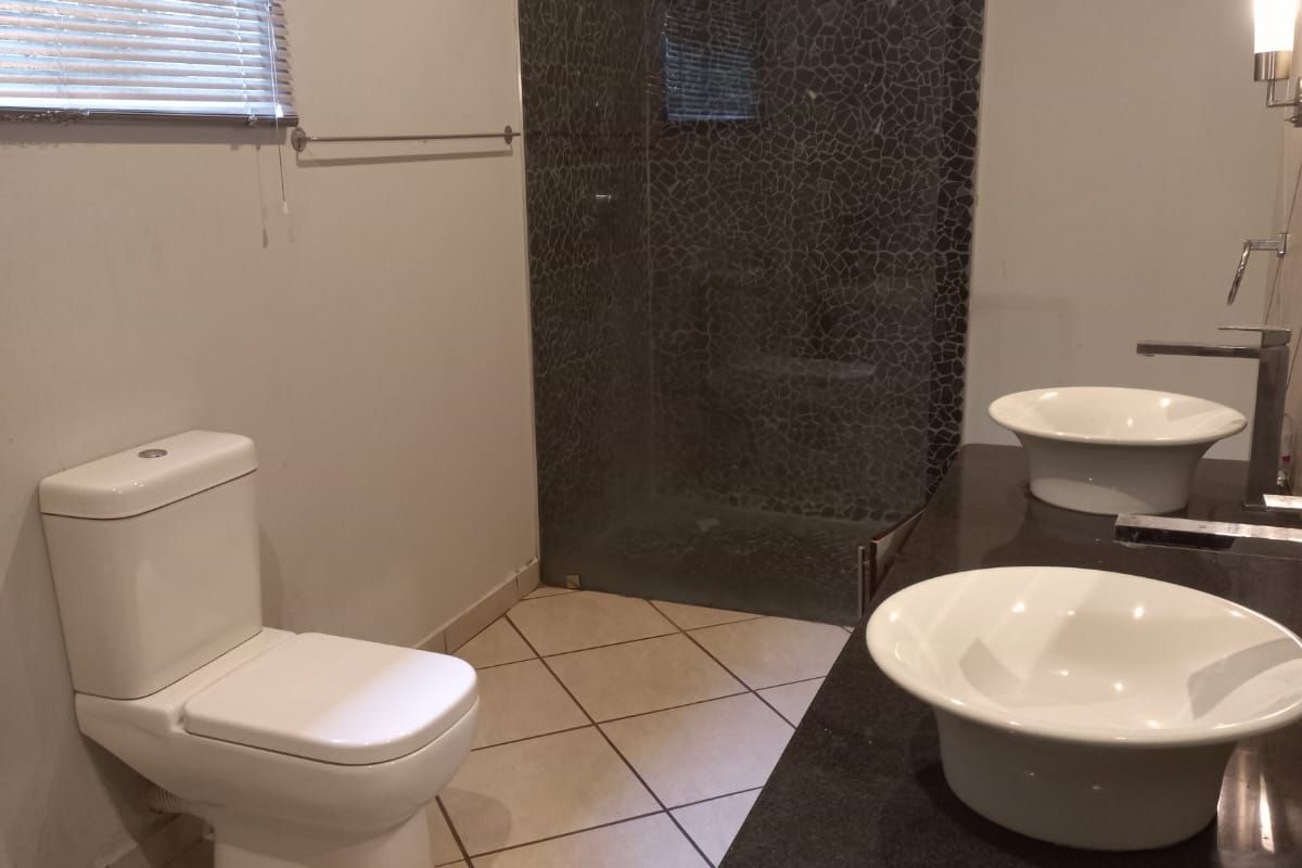 A functional bathroom featuring a double vanity with vessel sinks, a walk-in shower with mosaic tile detailing, and a modern toilet.