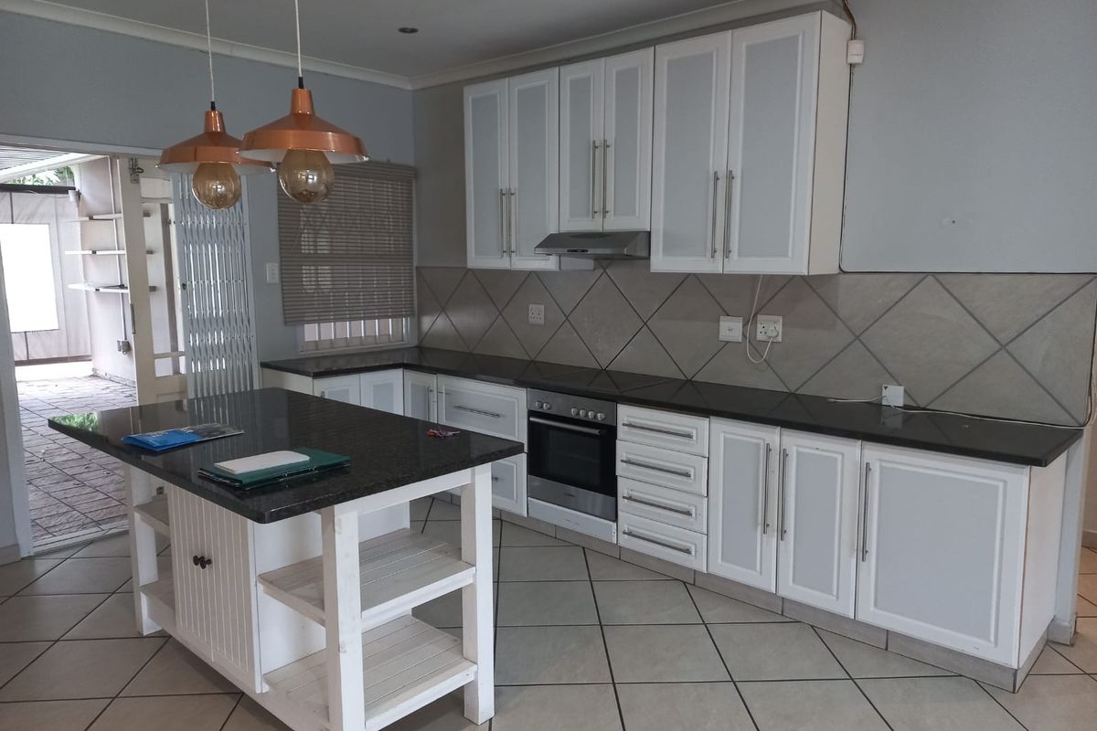 Modern kitchen featuring white cabinetry, dark granite countertops, a central island, built-in oven, extractor fan, and tiled flooring with direct access to the patio.