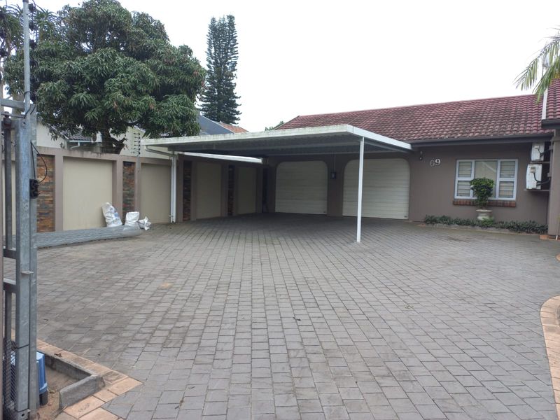 Front exterior view featuring a paved driveway, double garage with roll-up doors, and a covered carport area.