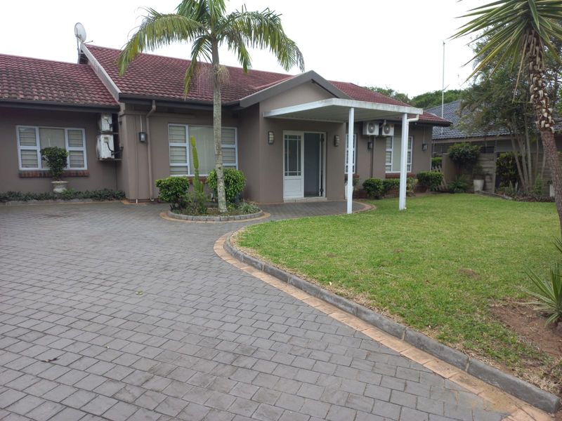 Front exterior view of a single-story house featuring a paved driveway, manicured lawn, and a covered entrance patio.