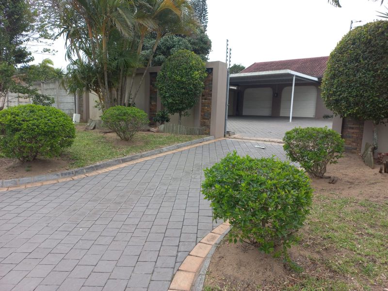 A paved driveway leading to a double garage with a carport, featuring landscaped garden beds and perimeter walling.
