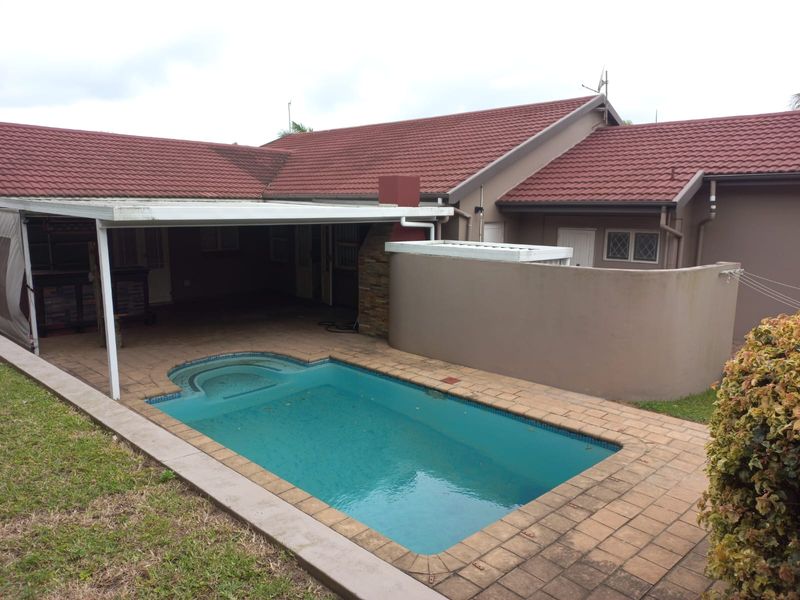 Rear exterior view featuring a swimming pool with paved surround and a covered patio area attached to the main house structure.